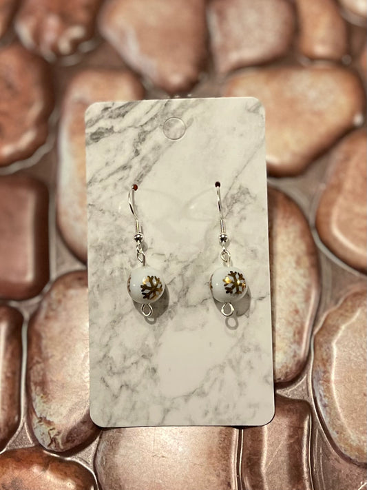 Pair of Sterling Silver Christmas earrings. Dangle/Drop style earrings with gold snowflakes on a white bead. Pictured on a marble earring card with a stone background.