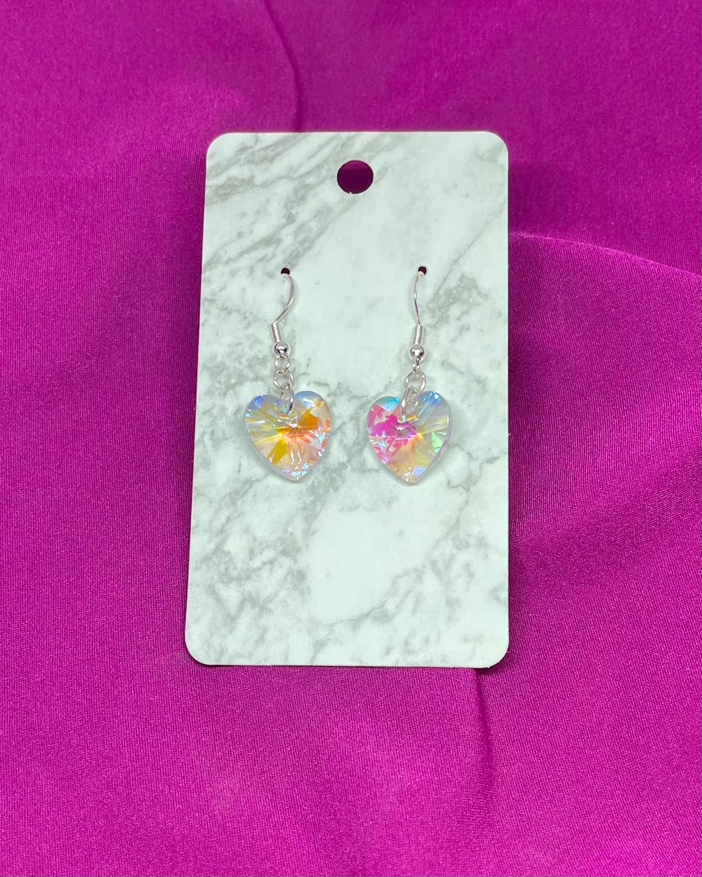 Heart-shaped earrings on a marble card with a pink background