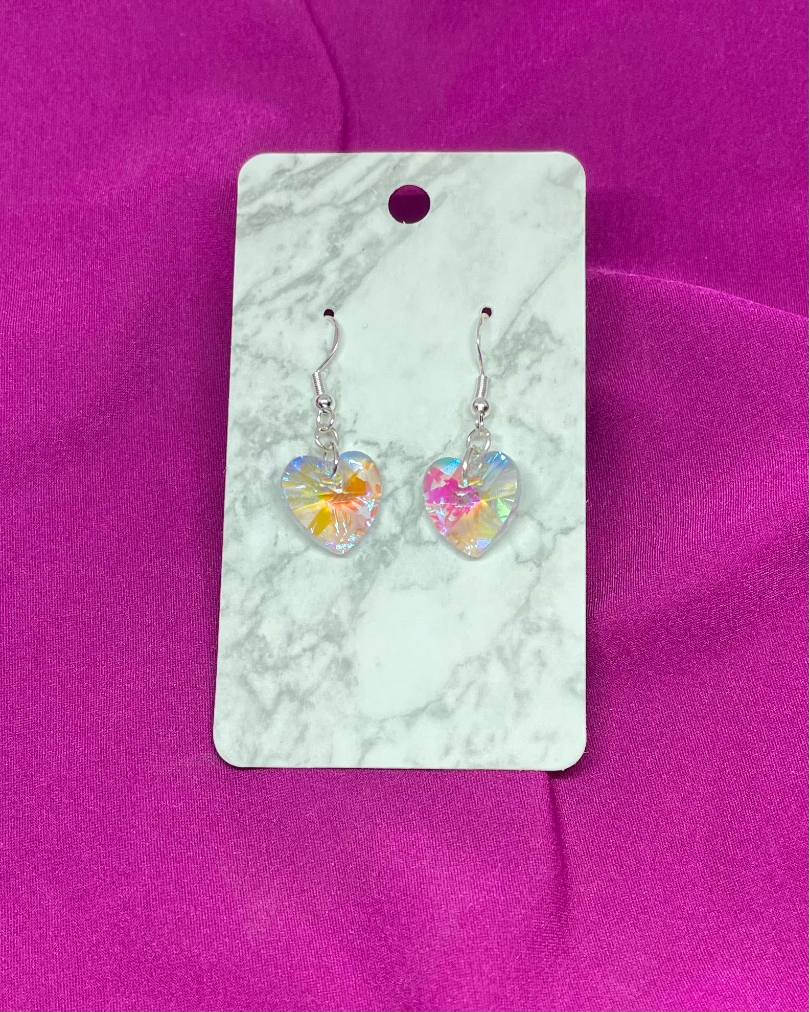 Heart-shaped earrings on a marble card with a pink background