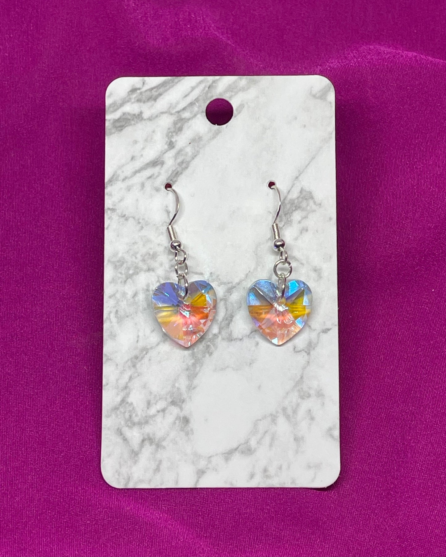 Heart-shaped earrings on a marble card with a pink background