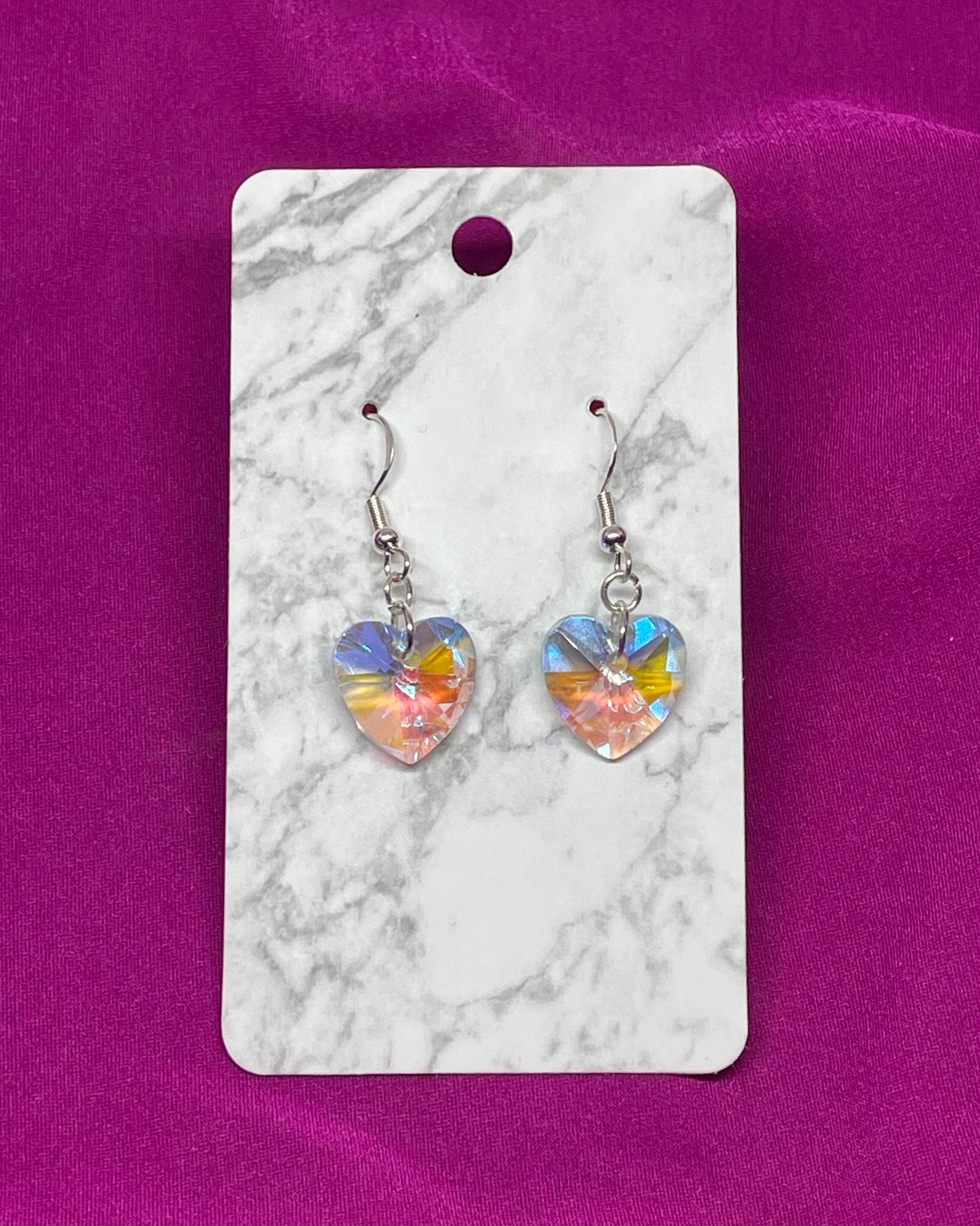Heart-shaped earrings on a marble card with a pink background